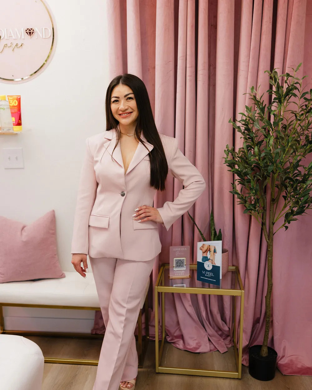 Leslie at reception in a blush suit, the round Pink Diamond logo on the wall behind her